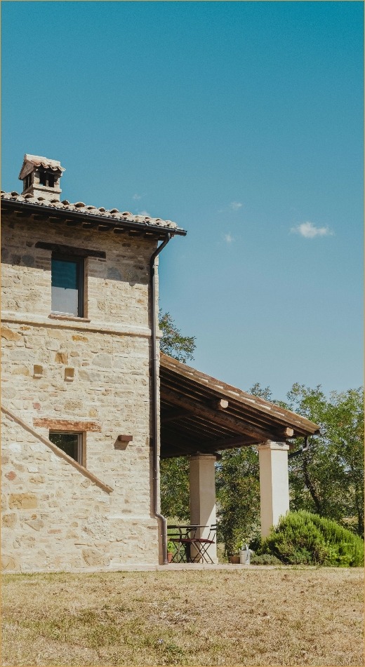 Maison en pierre avec toit en tuiles sous un ciel bleu clair, entourée d'un jardin herbeux